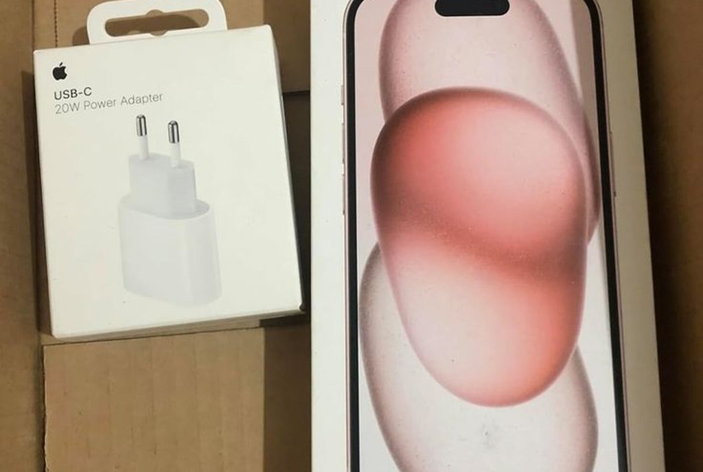 Caixa de papelão com um celular lacrado e um carregador de parede na embalagem original