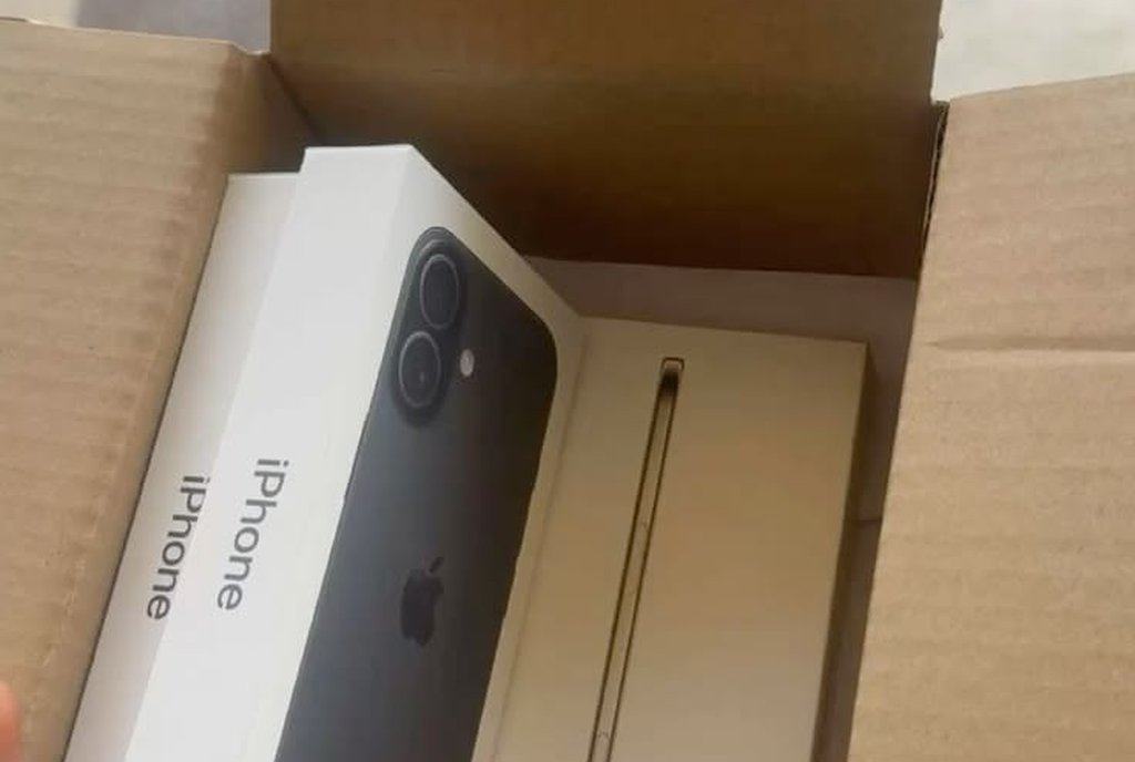 Caixa de papelão aberta com uma caixa de celular lacrada dentro, sobre uma mesa
